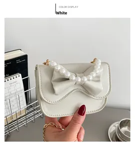 Close-up of white bow handbag featuring elegant pearl handle and gold chain details