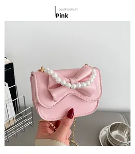 Pink mini leather bag with pearl handle and bow design shown with gold chain strap