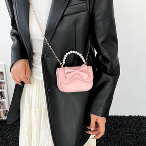 Pink PU leather crossbody bag with pearl handle and bow decoration worn by model