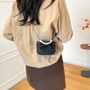 Chic black mini bag with pearl handle and bow detail worn as a stylish crossbody bag