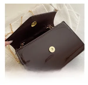Detail show of dark brown patent leather bag with gold chain and magnetic buckle closure
