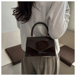 Detail of dark brown patent leather mini bag with gold chain strap and top handle