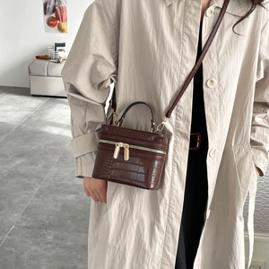 Brown crocodile embossed box bag with gold zipper and top handle shown on a trench coat