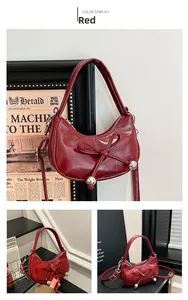 Detail of burgundy crescent handbag with glossy patent leather finish and bow accent