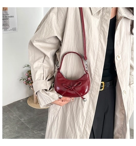 Close-up of a burgundy semi-circle handbag with a decorative bow and silver sphere charm