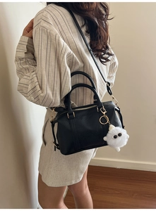 Close-up of black leather Boston bag with gold hardware and white plush monster charm
