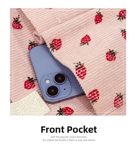 Detail of pink corduroy tote bag featuring a red strawberry print and functional front pocket