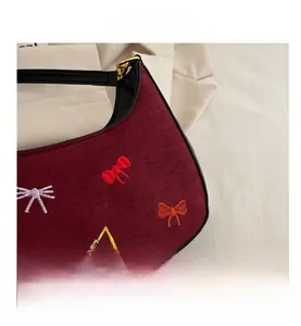 Détail d'un sac à bandoulière en daim bordeaux avec broderie de nœuds colorés et métal doré