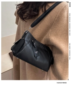 Detail of black faux leather shoulder bag featuring a functional side pocket and silver hardware