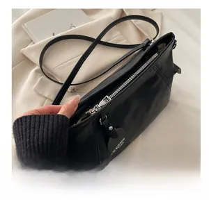 Detailed close-up of smooth silver metal zipper on minimalist black leather shoulder bag