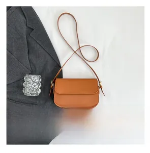 Sac bandoulière en cuir marron à côté d'un smartphone pour illustrer sa taille compacte