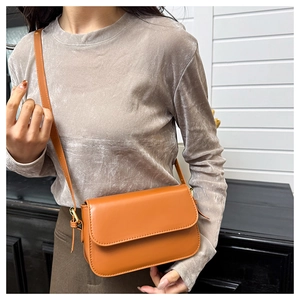 Gros plan d'un sac bandoulière en cuir marron caramel avec boucle dorée sur un mannequin