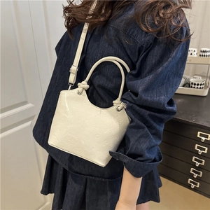 White embossed bucket bag with adjustable strap shown worn on shoulder in a lifestyle setting