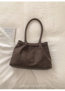 Top view of a minimalist deep brown suede tote bag on a textured white linen background