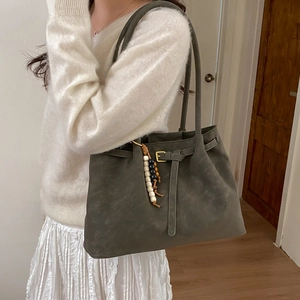 Matte dark grey tote bag with wooden bead charm worn by a model in a minimalist room