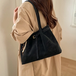 Vintage black faux suede tote bag with belt buckle and wooden bead charm on a beige coat