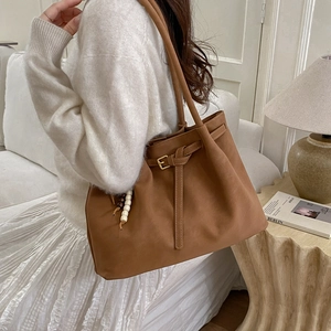 Detail of caramel leather tote bag featuring a decorative buckle and stylish beaded charm