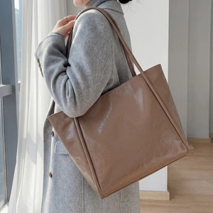 Close-up of a large brown glossy patent leather tote bag on a model's shoulder