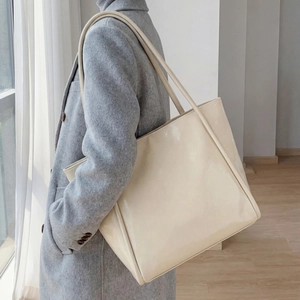 Detail of glossy cream tote bag showing premium patent leather texture on a model shoulder
