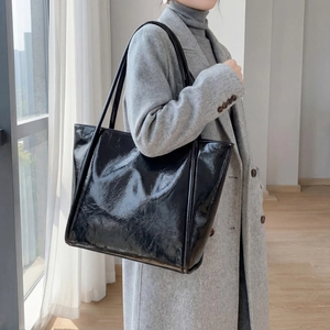 Detail showing high-gloss black tote bag texture and reinforced stitching on shoulder strap