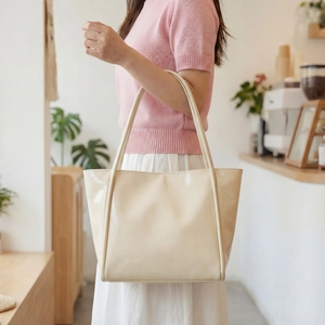 Chic cream white high-gloss tote bag shown in a cozy cafe setting being held by a model