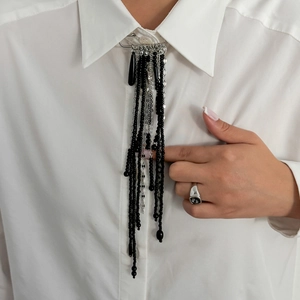 Détail d'une longue broche à franges en perles noires et chaînes argentées sur un col