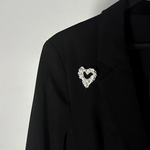 Dettaglio di una spilla a cuore d'argento con trama lavica su un bavero nero