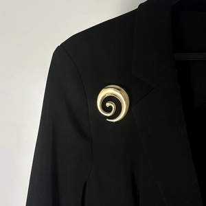 Dettaglio di una spilla dorata a spirale con pieghe irregolari su un revers nero