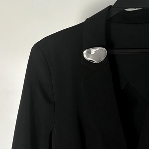 Dettaglio di una spilla in metallo liquido sul bavero di un abito nero per un look di lusso