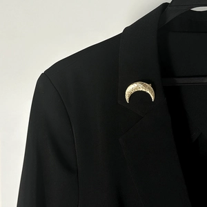 Dettaglio ravvicinato della spilla a mezzaluna dorata con texture martellata su blazer