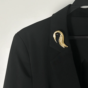 Dettaglio ravvicinato di una spilla in metallo dorato testurizzato su un blazer nero