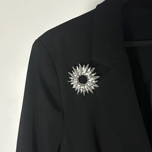 Détail d'une broche argentée irrégulière en forme de soleil sur un revers de veste