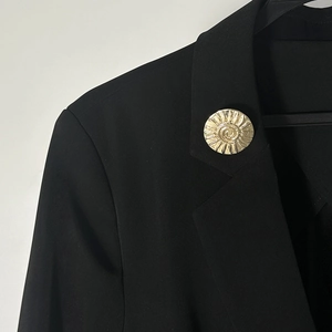 Dettaglio di una spilla dorata con trama a spirale sul risvolto di un blazer nero