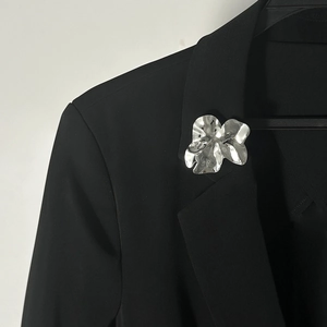 Dettaglio di una spilla a fiore argento liquido su un bavero di abito nero