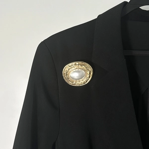 Dettaglio della spilla dorata stropicciata con perla sul risvolto di un blazer nero