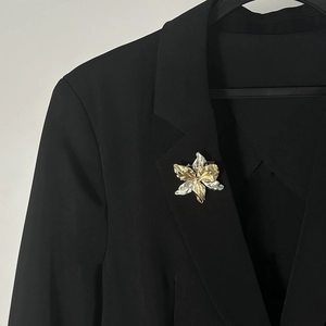Dettaglio di una spilla floreale bicolore con trama in metallo pieghettato su un blazer