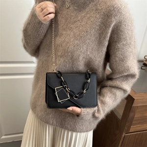 Elegant black chain crossbody bag with gold geometric buckle on beige knitwear outfit