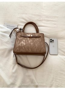 Detail view of retro brown textured square bag with golden twist lock and baseball charm