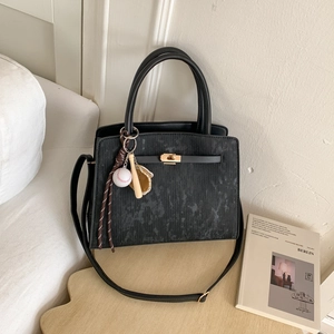Black marble-textured handbag on wooden table featuring baseball charm and golden clasp