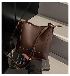 Close-up of dark brown leather bucket bag texture and stitching on a modern backdrop