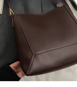 Detail view of the brown leather bucket bag showing stitching and golden metal hooks