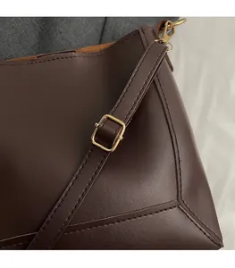 Detail of adjustable shoulder strap with gold-tone buckle on dark brown bucket bag