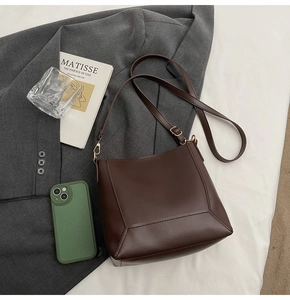 Detail of a vintage dark brown leather bucket bag on a suit with lifestyle accessories