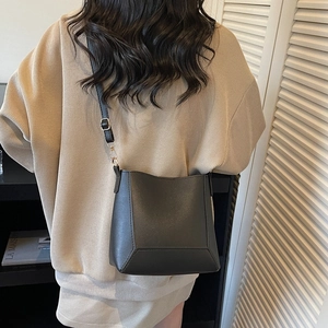 Minimalist black leather bucket bag shown on shoulder with adjustable strap and metal buckle
