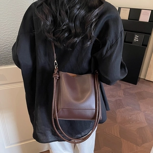 Brown leather bucket bag with tie detail and adjustable shoulder strap worn by model