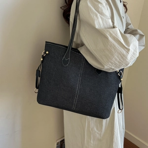 Black denim tote bag with contrast stitching and gold hardware shown on a model