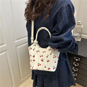 White cherry print tote bag with adjustable strap worn with denim outfit in indoor setting