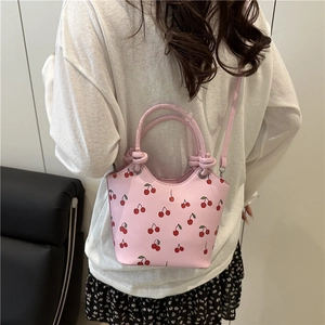 Pink bucket bag with red cherry print worn by model showing crossbody style