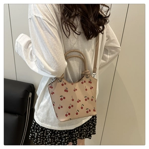 Lifestyle view of a beige bucket bag with cherry print shown on a model's shoulder