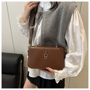 Brown leather crossbody bag with gold horseshoe buckle styled on a model's shoulder